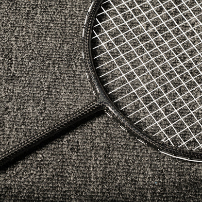 Close-up of a carbon fiber badminton racket showcasing the distinct carbon fiber texture on the frame and shaft, with white strings, laid on a gray textured surface.