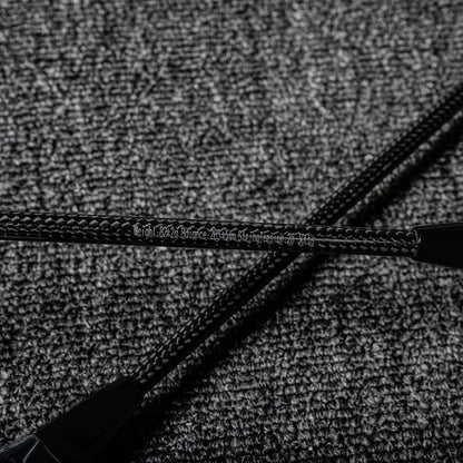 Close-up of two carbon fiber badminton racket shafts showcasing their distinct textured pattern and printed specifications, crossed on a gray textured surface.