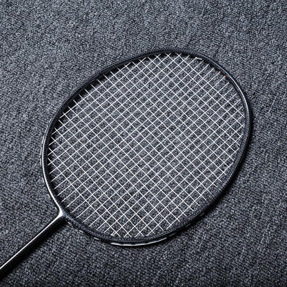 Close-up of a carbon fiber badminton racket with a black frame and white strings, laid on a gray textured surface.