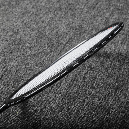 Close-up of a carbon fiber badminton racket frame showcasing its textured surface and white strings, positioned on a gray textured background.