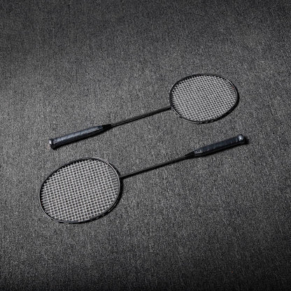 Close-up of two carbon fiber badminton rackets with black frames and white strings, laid on a gray textured surface.