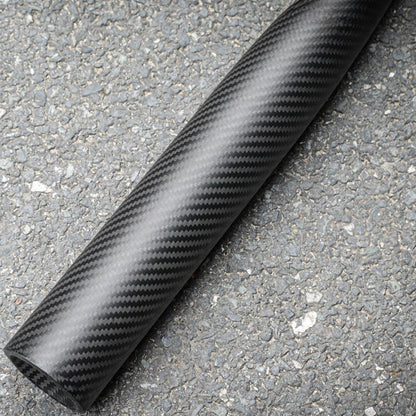 Close-up of a 3K carbon fiber baseball bat with a distinct weave pattern, placed on an asphalt surface.