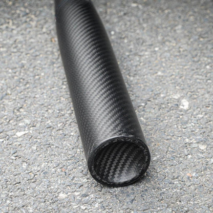 Close-up of a 3K carbon fiber baseball bat with a distinct weave pattern, showcasing the end and body detail, placed on an asphalt surface.