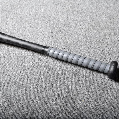 Close-up of the handle of a forged carbon fiber baseball bat, featuring a gray textured grip, laid on a gray textured surface.