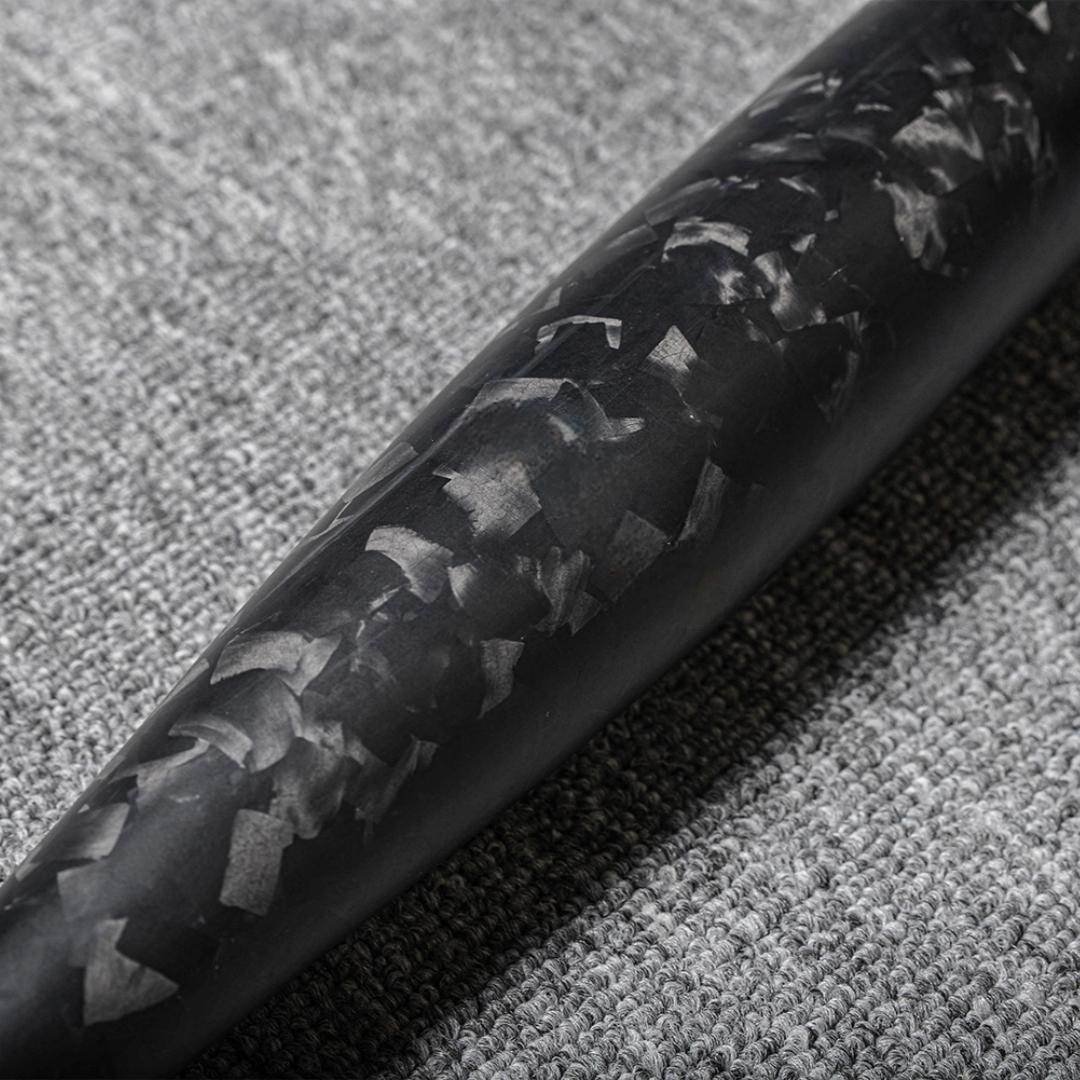Close-up of a forged carbon fiber baseball bat showcasing the distinct chopped carbon fiber pattern, placed on a gray textured fabric surface.