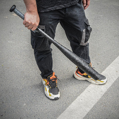 A person holding a forged carbon fiber baseball bat with a distinct chopped carbon fiber pattern, positioned on an asphalt surface.