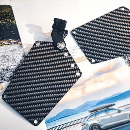 Close-up of two carbon fiber bicycle number plates with a distinct woven pattern, one featuring a mounting clip, displayed against a backdrop with automotive and landscape imagery.