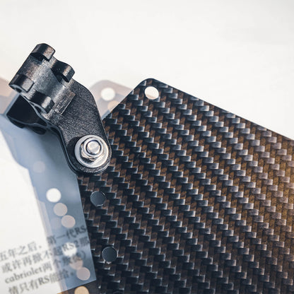 Close-up of a carbon fiber bicycle number plate showcasing its distinct woven carbon fiber pattern and a metal mounting component with a bolt.