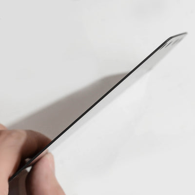 Close-up side view of a carbon fiber bicycle number plate, showcasing its thin profile, held by a hand against a white background.