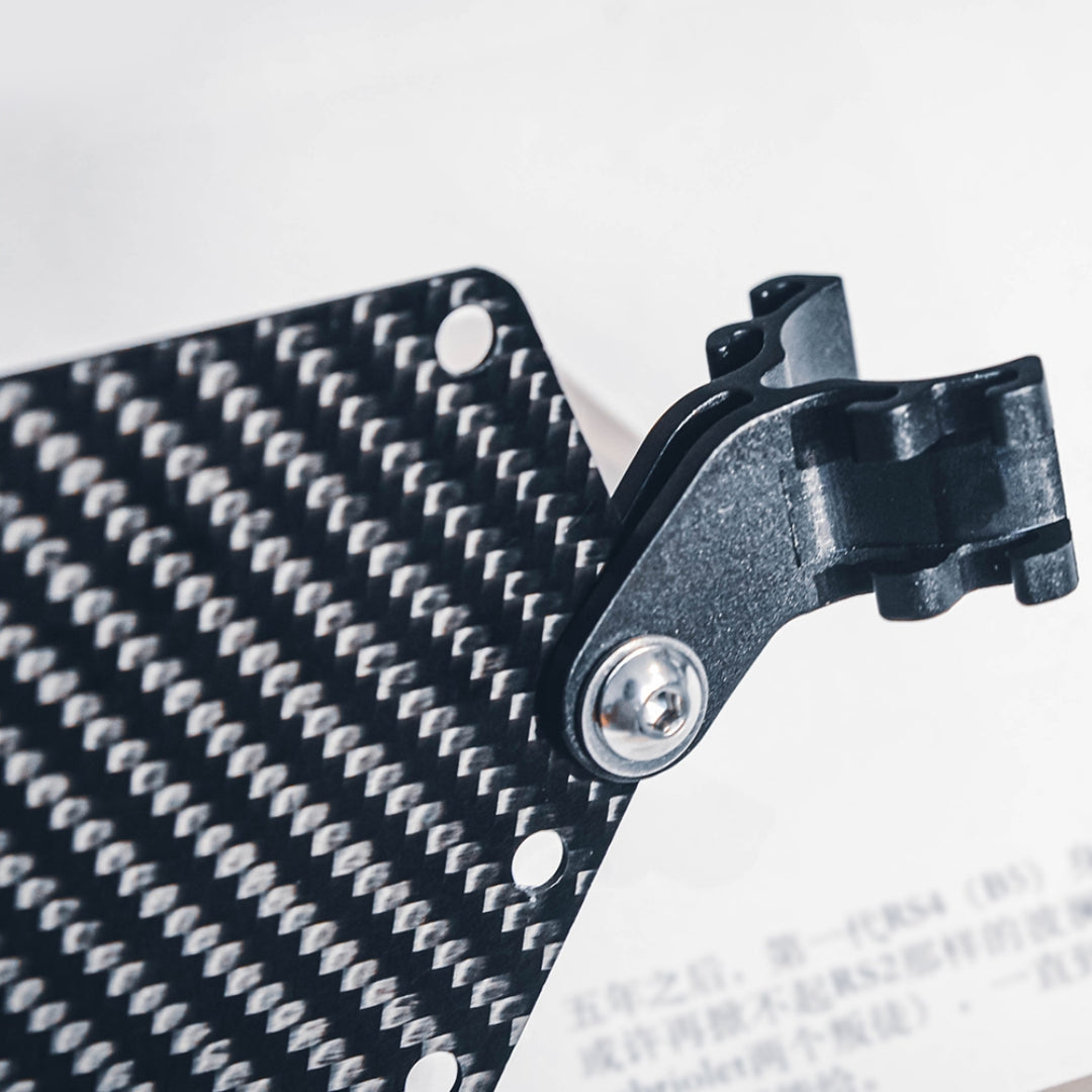 Close-up of a carbon fiber bicycle number plate showcasing its distinct woven pattern and a metal mounting bracket with a screw.