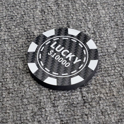 Close-up of a poker chip-style carbon fiber bottle opener with "LUCKY $10000" text, showcasing its carbon fiber texture, placed on a gray textured surface.