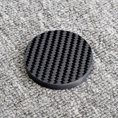 Close-up of a 3K carbon fiber bottle opener with a distinct woven pattern, showcasing its circular shape and glossy finish, placed on a gray textured surface.