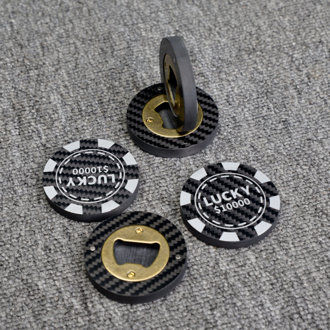 Close-up of multiple carbon fiber bottle openers, including poker chip-style ones with "LUCKY $10000" text and designs featuring brass bottle opener mechanisms, displayed on a gray textured surface.