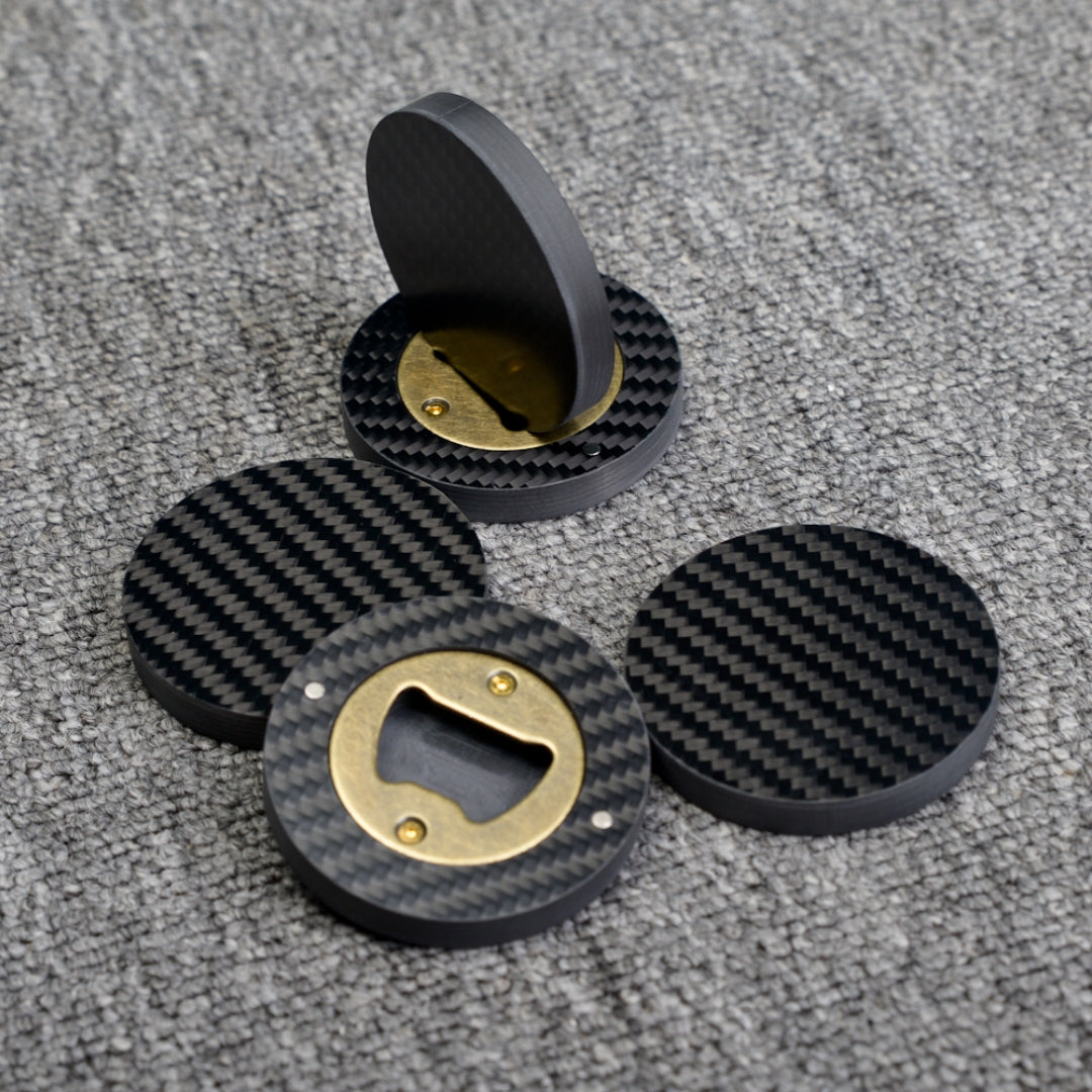 Close-up of multiple 3K carbon fiber bottle openers with brass opener mechanisms, showcasing their circular shape and distinct woven carbon fiber pattern, placed on a gray textured surface.