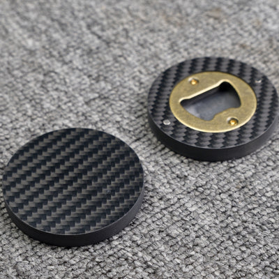 Close-up of two 3K carbon fiber bottle openers, showcasing their circular shape, distinct woven carbon fiber pattern, and brass opener mechanism