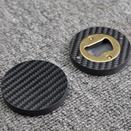 Close-up of two 3K carbon fiber bottle openers, showcasing their circular shape, distinct woven carbon fiber pattern, and brass opener mechanism, placed on a gray textured surface.