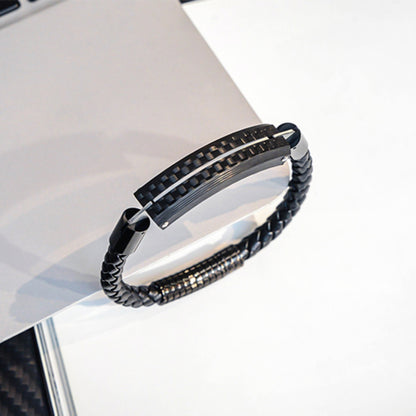Close-up detail of a carbon fiber bracelet featuring a black braided strap and metallic accents, resting on a light-colored surface.