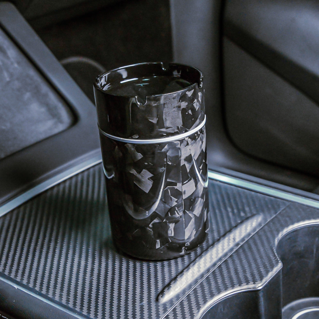 Close-up of a forged carbon fiber car ashtray with a distinct patterned texture, placed on a carbon fiber-trimmed center console in a vehicle.