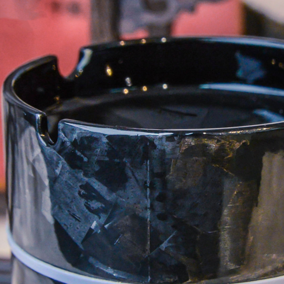 Close-up detail of a forged carbon fiber car ashtray, showcasing its distinct fragmented pattern, glossy finish, and cigarette rest design.