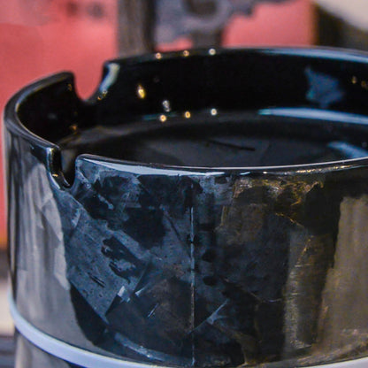 Close-up detail of a forged carbon fiber car ashtray, showcasing its distinct fragmented pattern, glossy finish, and cigarette rest design.