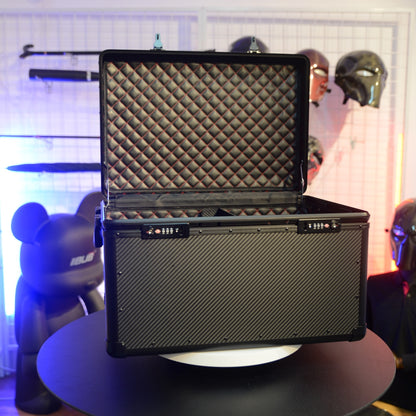 Close-up detail of an open 3K carbon fiber car trunk storage case with combination locks, featuring a quilted interior with red stitching, placed on a round table against a decorative background with figurines and masks.