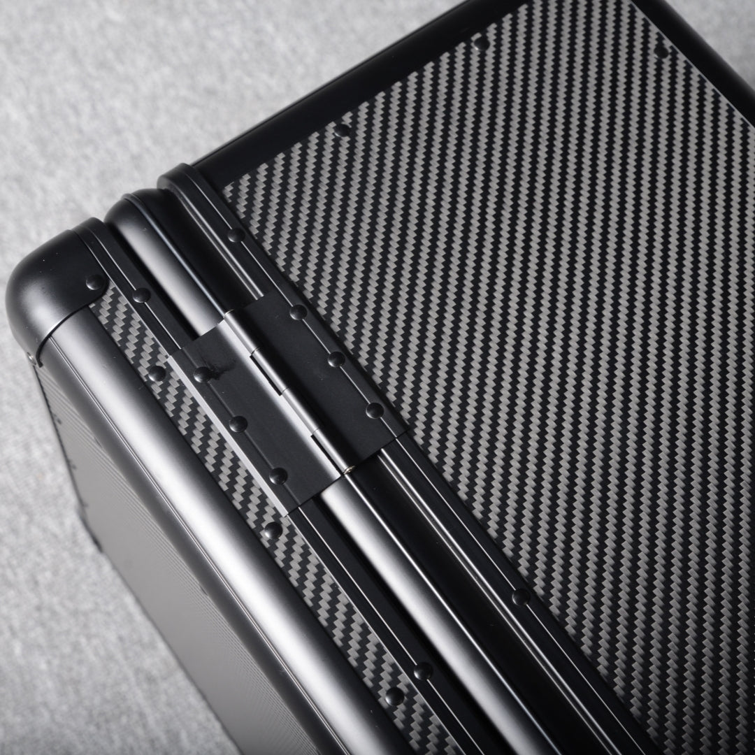 Close-up detail of a 3K carbon fiber large car storage trunk, showcasing the hinge and distinctive woven pattern, placed on a gray textured surface.