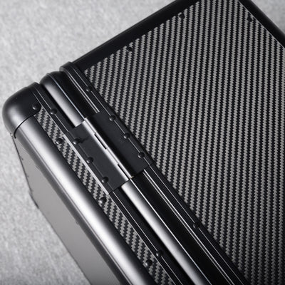 Close-up detail of a 3K carbon fiber large car storage trunk, showcasing the hinge and distinctive woven pattern, placed on a gray textured surface.