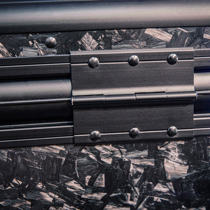 Close-up detail of the back side of a large forged carbon fiber car storage trunk, highlighting the chopped carbon fiber pattern and a metal hinge with rivets.
