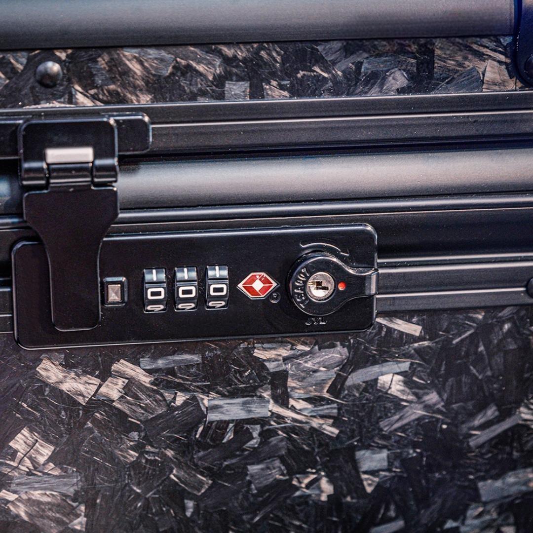 Close-up detail of the combination lock with TSA logo on the bottom part of a large forged carbon fiber car storage trunk, showcasing the chopped carbon fiber pattern.