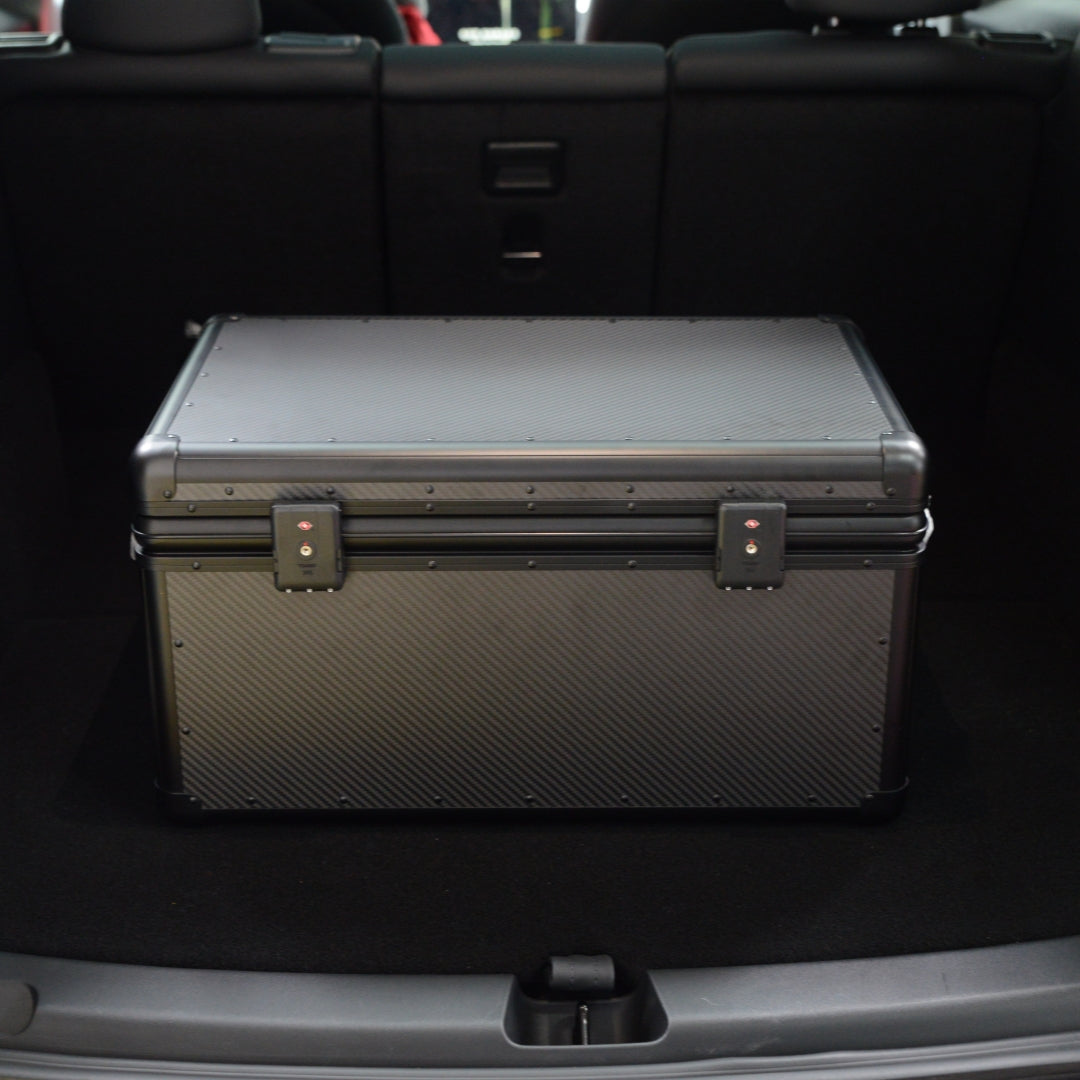 Close-up of a closed large 3K carbon fiber car storage trunk with metallic locks, placed in a car trunk.