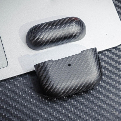 Close-up of 3K carbon fiber AirPods cases showcasing the distinct weave pattern, displayed on a surface with matching carbon fiber texture and a metallic background.