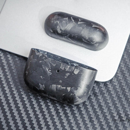 Close-up of forged carbon fiber AirPods cases showcasing the unique marbled texture, displayed on a surface with a carbon fiber pattern and a metallic background.