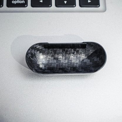 Close-up of the interior of the top half of a 3K carbon fiber AirPods case, showcasing the distinct weave pattern, placed on a metallic surface with a keyboard in the background.
