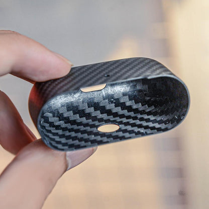 Close-up of the interior of the lower half of a 3K carbon fiber AirPods case, showcasing the distinct weave pattern, held in a hand against a soft background.