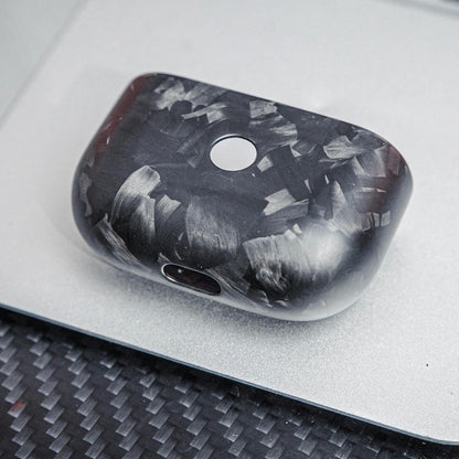 Close-up of the front side of the lower half of a forged carbon fiber AirPods case, showcasing its unique marbled texture, placed on a silver surface with a carbon fiber textured background.
