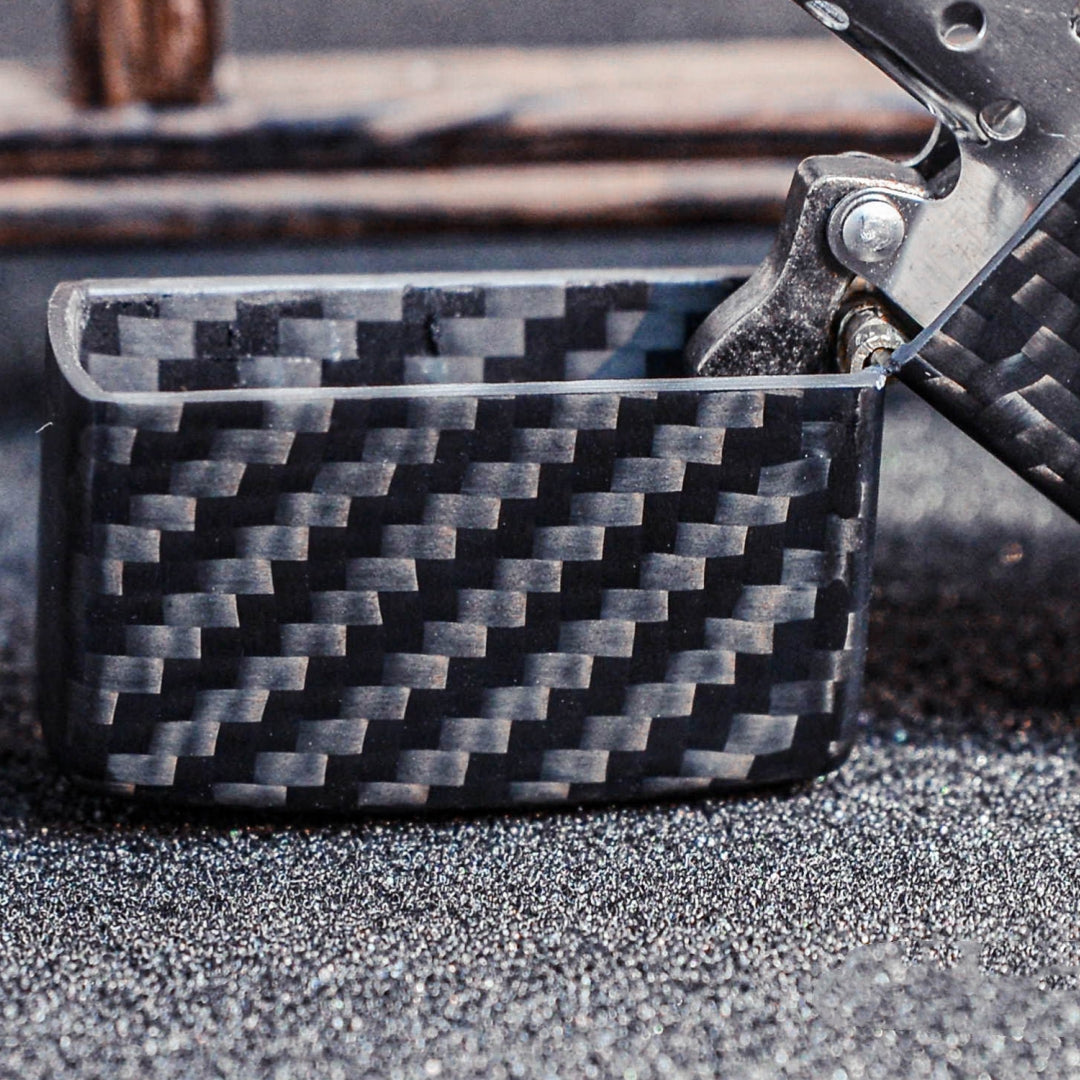 Close-up of an open 3K carbon fiber Zippo lighter case showcasing the detailed weave pattern, placed on a textured glittery dark surface.
