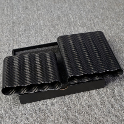 Close-up of two carbon fiber cigar tubes (each capable of holding 5 cigars) with a distinct weave pattern, placed in an open black box on a gray fabric surface.
