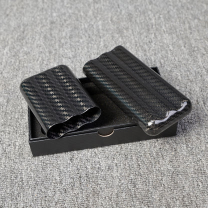 Close-up of carbon fiber cigar tubes with a capacity for 3 cigars, featuring a distinct weave pattern, placed in a black box on a gray fabric surface.