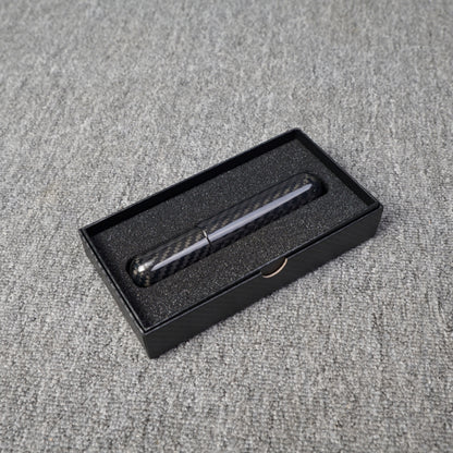 Close-up of a carbon fiber cigar tube with single cigar capacity, featuring a distinct weave pattern, placed in a black box with foam lining on a gray fabric surface.