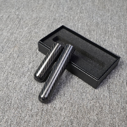 Close-up of two carbon fiber cigar tubes with single-cigar capacity, featuring a distinct woven pattern, placed near an open black box with foam lining on a gray fabric surface.