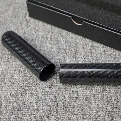 Close-up of a carbon fiber cigar tube (single-cigar capacity) with a distinct woven pattern, displayed in a disassembled state, placed on a gray fabric surface with a partial view of a black box in the background.