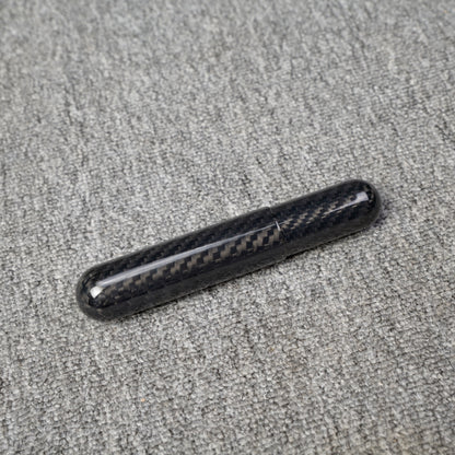 Close-up of a carbon fiber cigar tube with single-cigar capacity, featuring a distinct woven pattern, placed on a gray fabric surface.