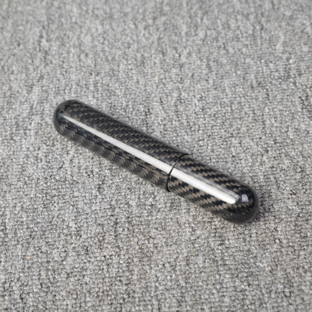 Close-up of a carbon fiber cigar tube with single-cigar capacity, featuring a distinct woven pattern, placed on a gray fabric surface.