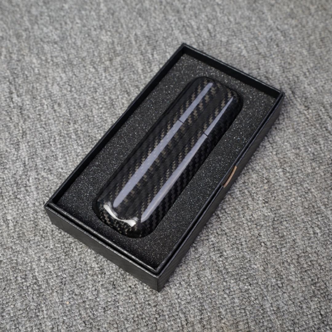 Close-up of a carbon fiber cigar case with a capacity for 2 cigars, featuring a distinct woven pattern, placed in an open black box with foam lining on a gray fabric surface.