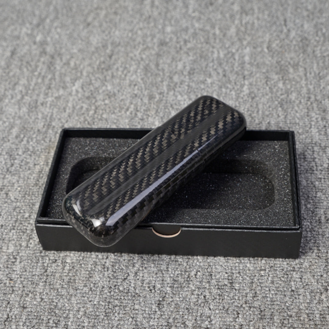 Close-up of a carbon fiber cigar case with a capacity for 2 cigars, featuring a distinct woven pattern, placed on an open black box with foam lining over a gray fabric surface.