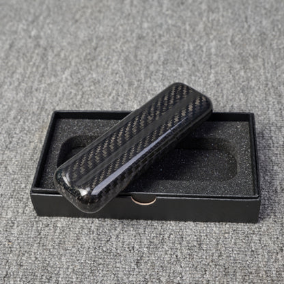 Close-up of a carbon fiber cigar case with a capacity for 2 cigars, featuring a distinct woven pattern, placed on an open black box with foam lining over a gray fabric surface.