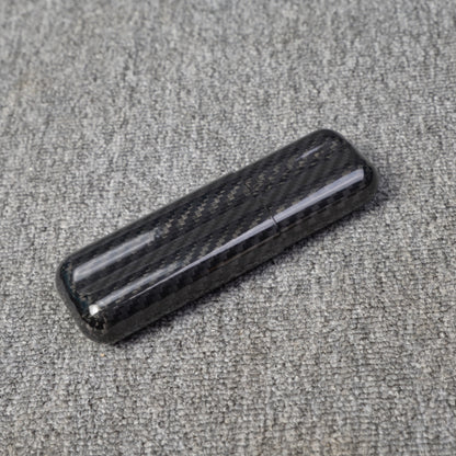 Close-up of a carbon fiber cigar case with a capacity for 2 cigars, featuring a distinct woven pattern, placed on a gray fabric surface.