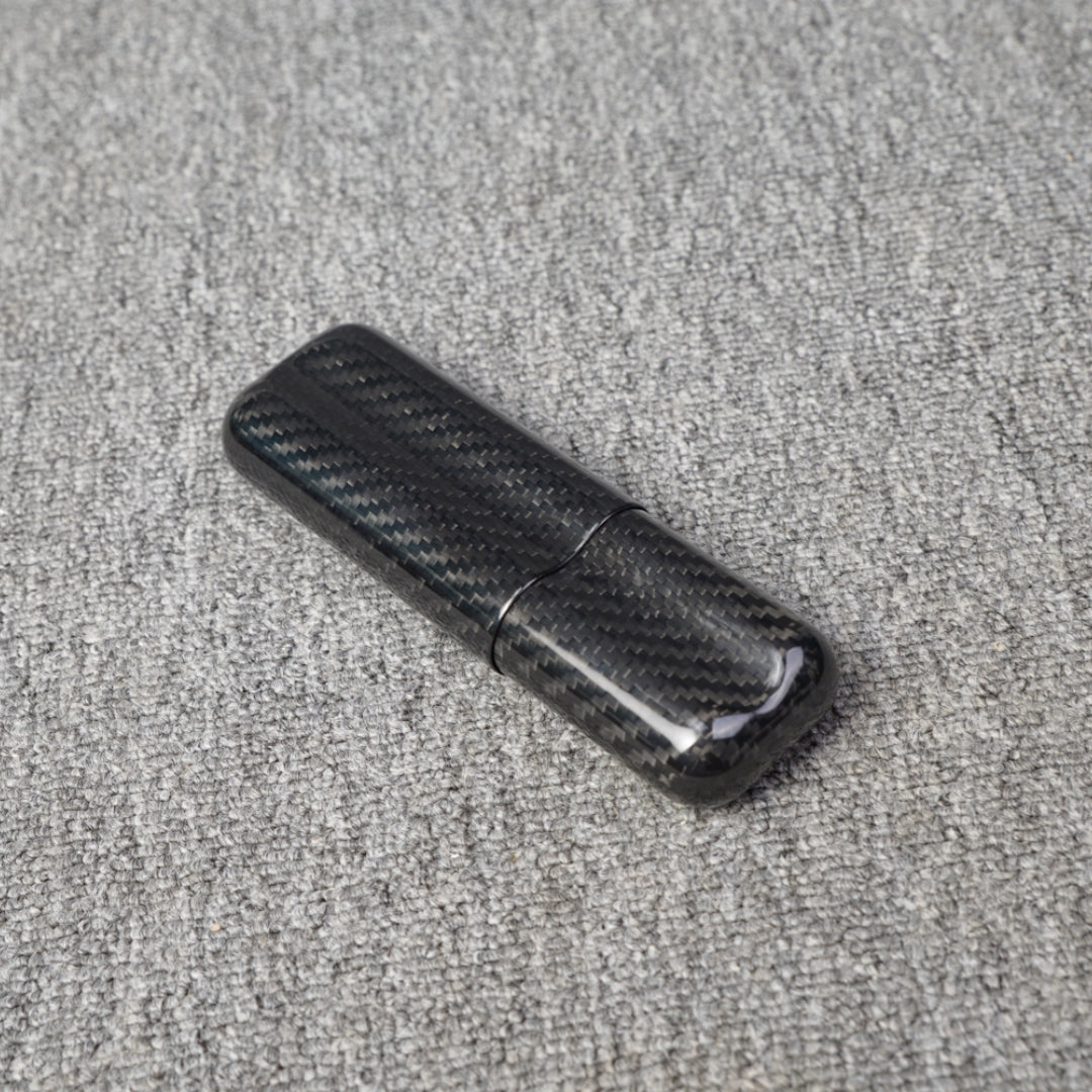 Close-up of a carbon fiber cigar case with a capacity for 2 cigars, featuring a distinct woven pattern, placed on a gray fabric surface.