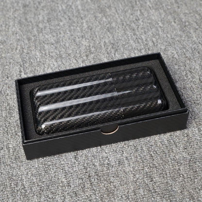 Close-up of a carbon fiber cigar tube with a capacity for 3 cigars, featuring a distinct woven pattern, placed in an open black box with foam lining on a gray fabric surface.
