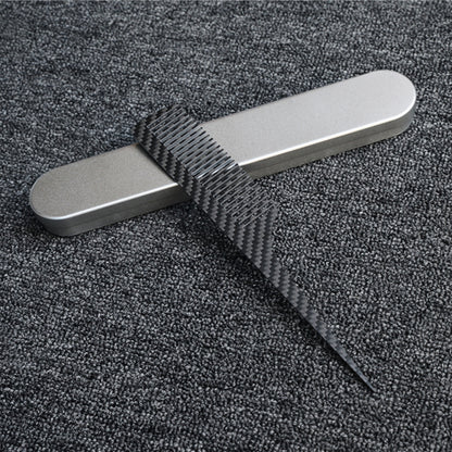 Close-up of a carbon fiber comb with a distinct woven pattern, placed next to a silver metal case on a dark gray textured fabric surface.